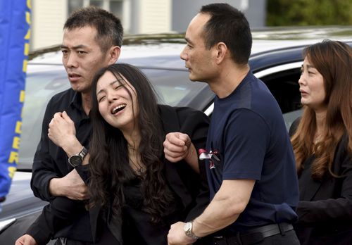 Peter Wang's mother Hui cries as she is helped to her car after the funeral for her son who was killed in the massacre. (AAP)