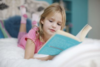 Young girl reading book on bed