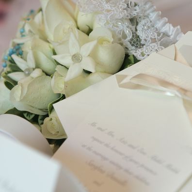Wedding invitation with following items in the background: bride's bouquet and  garter. Focus on the Bouquet and garter.
