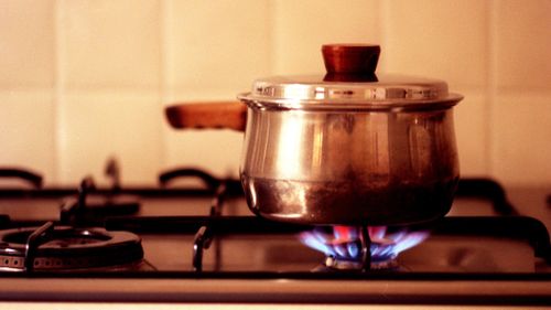 A gas flame burns under a pot on a gas stove top.