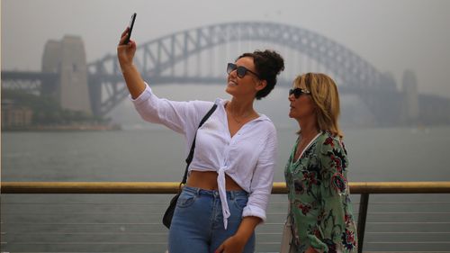 Duo take selfie outside Sydney Harbour Bridge as smoke shrouds the city.