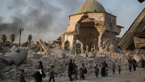 Fleeing Iraqi civilians walk past the heavily damaged al-Nuri mosque. (AAP)