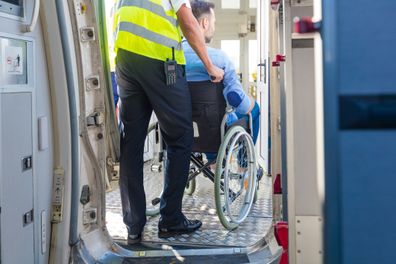 Ground service men helping wheelchair passenger to enter on airplane board, they using an elevator.