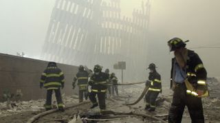 Feuerwehrleute arbeiten unter den zerstörten Pfosten, den vertikalen Streben, die einst die hoch aufragenden Außenwände der Türme des World Trade Centers verkleideten. (AAP)
