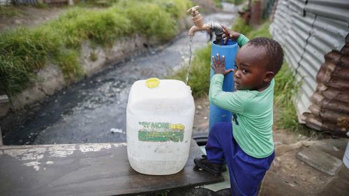 A little boy in Masiphumelele settlement in Cape Town fills out a container from a communal tap. (AAP)