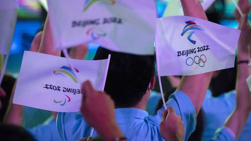 Participants wave flags with the logos of 2022 Beijing Winter Olympics and Paralympics before a launch ceremony to reveal the motto for the Winter Olympics and Paralympics in Beijing