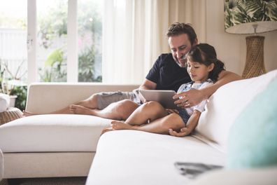 Father and daughter sitting on a sofa and using digital tablet.