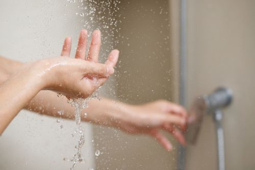 Una donna usa la mano per misurare la temperatura dell'acqua da uno scaldabagno prima di fare la doccia