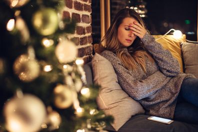 Depressed mid adult woman near christmas tree in her home.