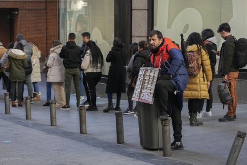 A lottery seller stands by a queue of people waiting to buy tickets from the Dona Manolita lottery shop, in Madrid, Spain, Wednesday, Dec. 20, 2023 