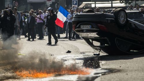 An UberPop vehicle overturned by French taxi drivers as they clash with riot police. (AAP)