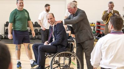 The Duke of Cambridge has his shoulders rubbed by the Prince of Wales after he attempted and failed to throw a basket ball into the hoop while playing wheelchair basket ball during a visit to the Defence Medical Rehabilitation Centre Stanford Hall