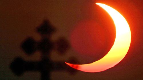 The rising sun is seen as a crescent over a cross in a graveyard on the Hohen Preissenberg, Bavaria, as it is partially hidden by the moon during a solar eclipse 31 May 2003. (Getty)