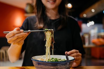 Image of an Asian woman eating a bowl of Japanese ramen using chopsticks in a Japanese ramen shop