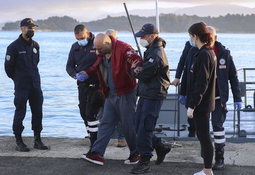 A slightly injured man helped by coast guard officers, arrives at the port of Corfu island, northwestern Greece, after the evacuation of a ferry, Friday, Feb. 18, 2022.