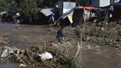 A man crosses a river at an informal settlement during flooding in Durban, South Africa, Thursday, April 14, 2022. 