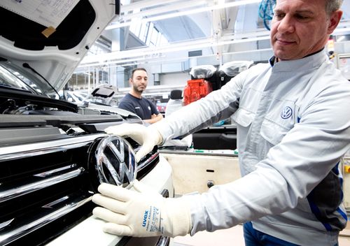 An employee displays a VW logo shortly before installation on a Volkswagen Touran in final assembly at the VW plant.