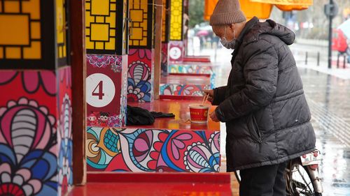 A man wearing a face mask to help protect against COVID-19 prepares to eat noodles on the street of Wuhan.