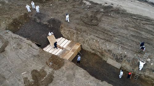 Workers wearing personal protective equipment bury bodies in a trench on Hart Island in New York.