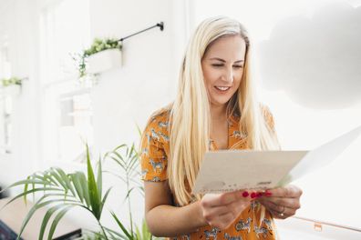 A front-view shot of a mid adult caucasian woman reading her birthday card in the office, she is smiling while reading birthday wishes from her co-workers.