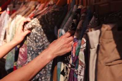 A woman is browsing a rail of clothes at an op shop