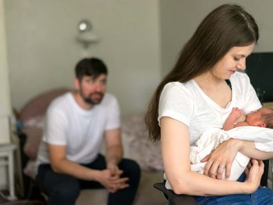 Mum breastfeeding while dad sits in left corner.