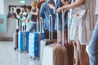 Travelers with luggage using smartphones while waiting in line for boarding at the airport. Focus on wheeled luggage.