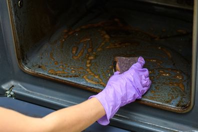 Close-up. Home cleaning concept. A woman's hand washes with a sponge on a dirty oven. Selective focus on hand