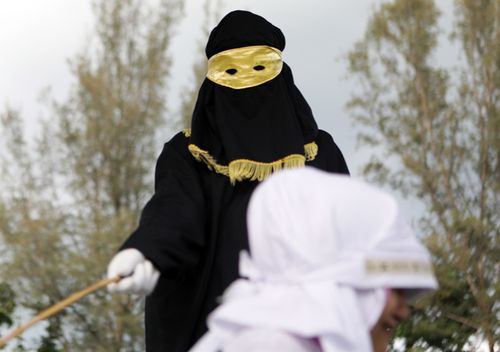 A sharia law enforcer, know as algojo, delivers a public punishment in Aceh, Indonesia. The Sharia Court in Aceh appoints those into the job of Algojo. With masked robes from head to foot to protect their identities, the algojo carry out punishments, including public whipping with a bamboo cane, as deemed by the court. 