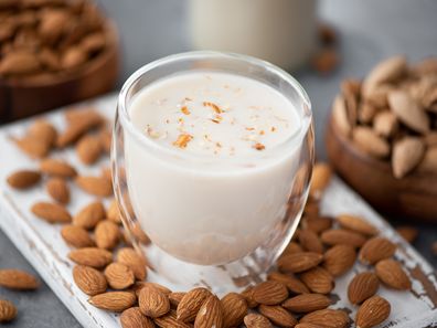 Homemade almond milk in a glass on a white wooden board.