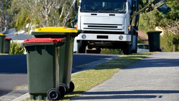 Focus on two Rubbish bins with rubbish truck in background lifting a bin