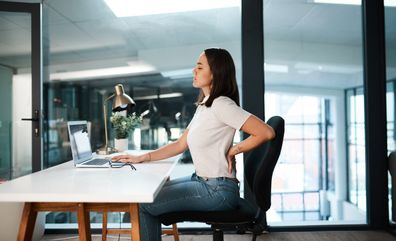 Shot of a young businesswoman experiencing back pain while working in an office