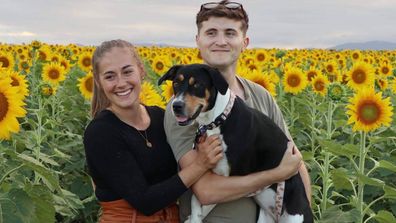 Talia and her partner in sunflower field carrying dog, Nala
