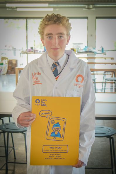 Josh Cowie wearing a lab coat and holding up his submission for the Little Big Ideas competition.