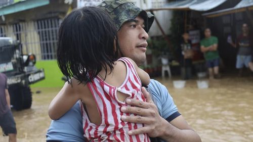 A rescuer carries a child to safer grounds as floods rose due to Tropical Storm Nalgae at Parang, Maguindanao province, southern Philippines on Friday Oct. 28, 2022. (Philippine Coast Guard via AP)