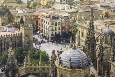 City of Seville, in the foreground the spires and domes of Seville cathedral, in the background an old town street with people moving about.