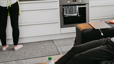 Woman in the kitchen while man sits on lounge