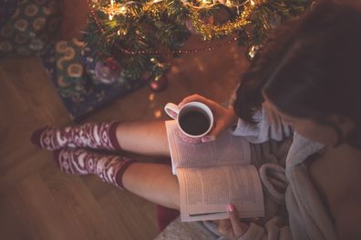 Girl by christmas tree with coffee cup reading a book
