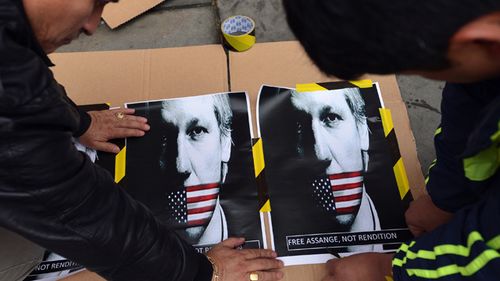 Supporters of WikiLeaks founder Julian Assange prepare a placard with posters showing Assange's portrait with a US flag over his mouth outside the Ecuadorian embassy in central London on June 21, 2012. Source: AFP