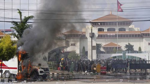 Riot police guard a parliament building while an ambulance burns during protests in Kathmandu, Nepal.