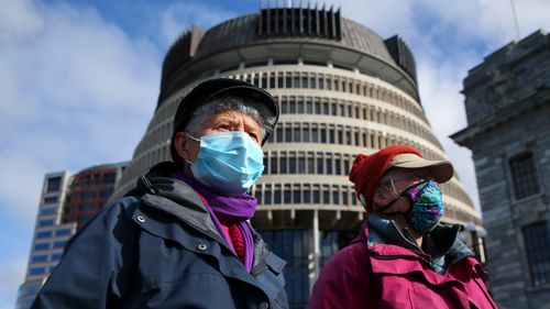 Two people in masks walk past the Beehive, New Zealand's parliament building in Wellington.