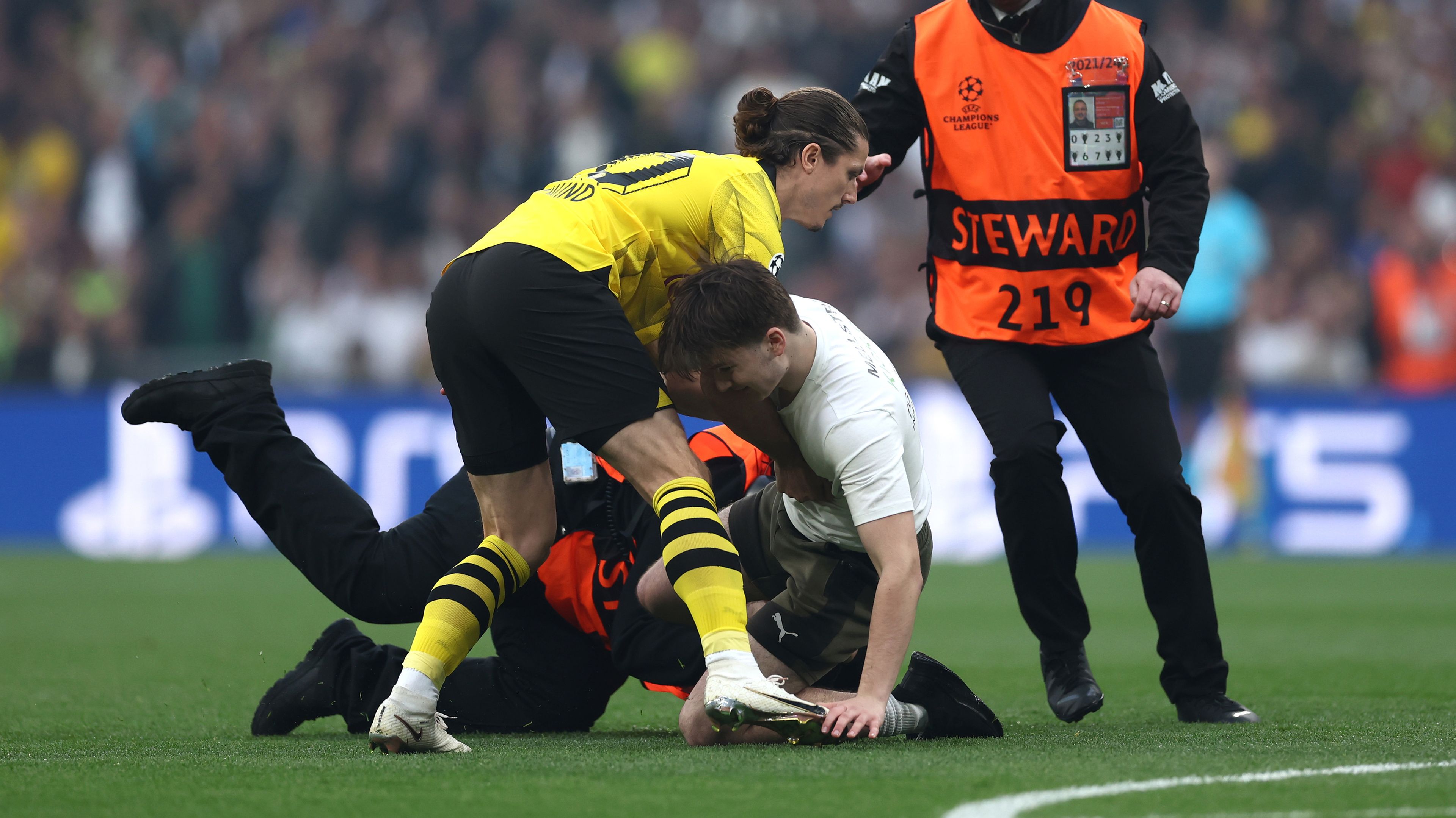 Marcel Sabitzer of Borussia Dortmund assists members of security as they stop a pitch invader.