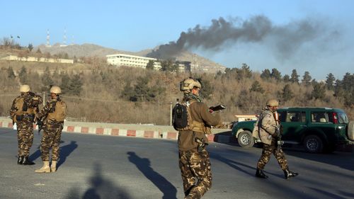 Afghan security personnel stand guard as black smoke rises from the Intercontinental Hotel. (AAP)
