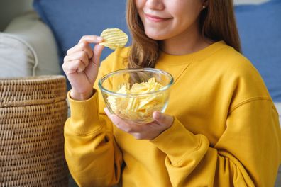 Closeup image of a young woman picking and eating potato chips at home