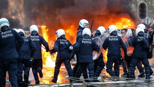 Riot police on the streets of Brussels as cars burn out of control during mass protests. (AAP)