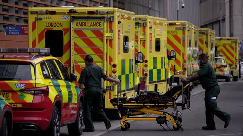 Paramedics push a trolley next to a line of ambulances outside the Royal London Hospital in the Whitechapel area of east London, Thursday, Jan. 6, 2022. 