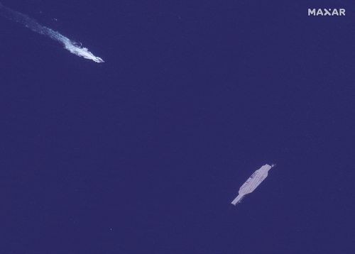 An Iranian fast boat, top left, approaches a mock-up aircraft carrier built by Iran, in the Strait of Hormuz.