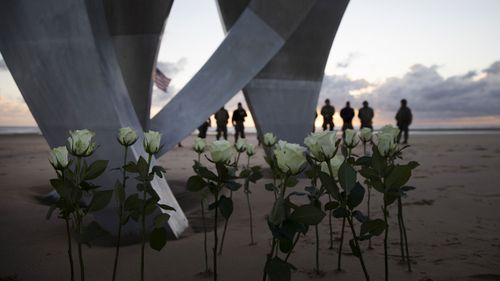Men in a vintage US WWII uniforms stand behind flowers left at Les Braves monument after a D-Day 76th anniversary ceremony in Saint Laurent sur Mer, Normandy, France, Saturday, June 6, 2020