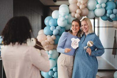 mom-to-be and her female best friend taking photos together with funny photo props at a baby shower