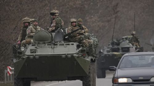 Ukrainian servicemen sit atop armored personnel carriers driving on a road in the Donetsk region.